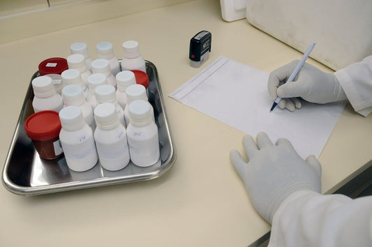 Provette per analisi di laboratorio e mano di medico che registra dati, simbolo dell’importanza di test per le malattie sessualmente trasmissibili.